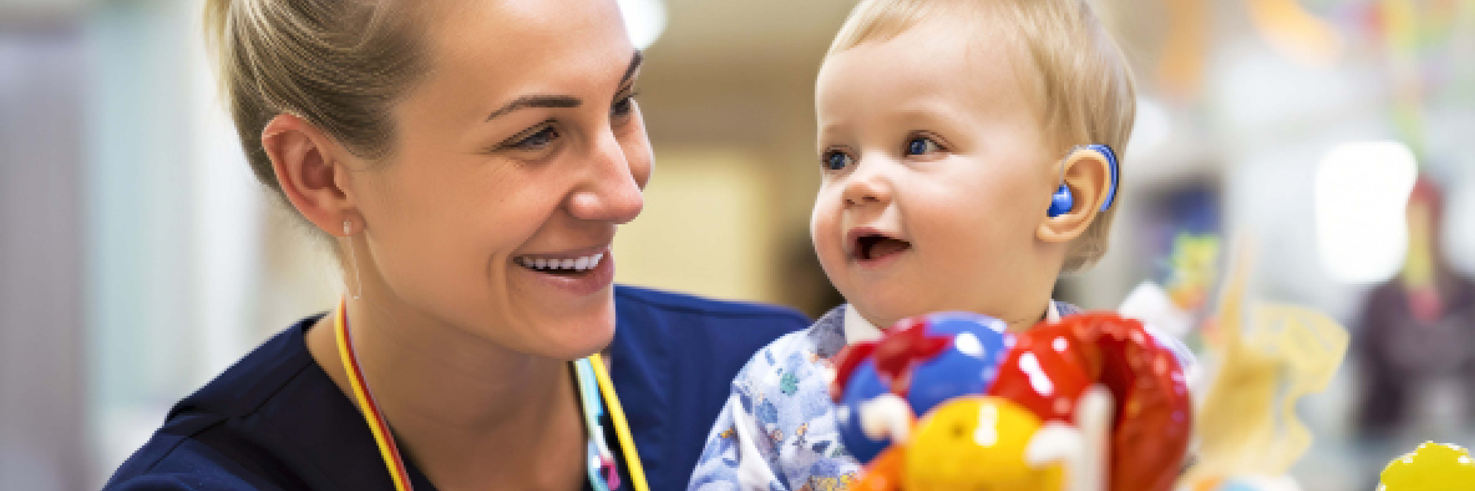 Healthcare worker smiling at an infant who is wearing a hearing aid