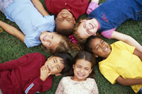 children of multiple races laying in the grass with their heads forming the center of a circle.
